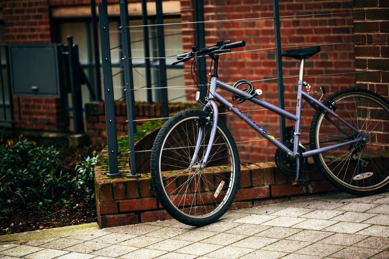 Purple bicycle propped up against some railings in front of a red brick building